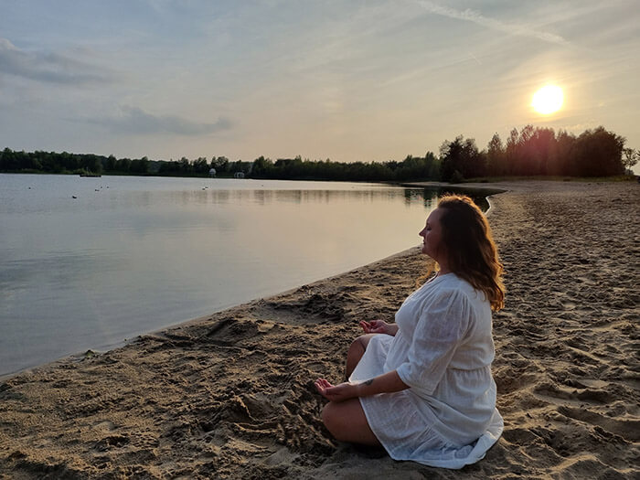 Sanne Udink zittend aan het water bij zonsondergang.